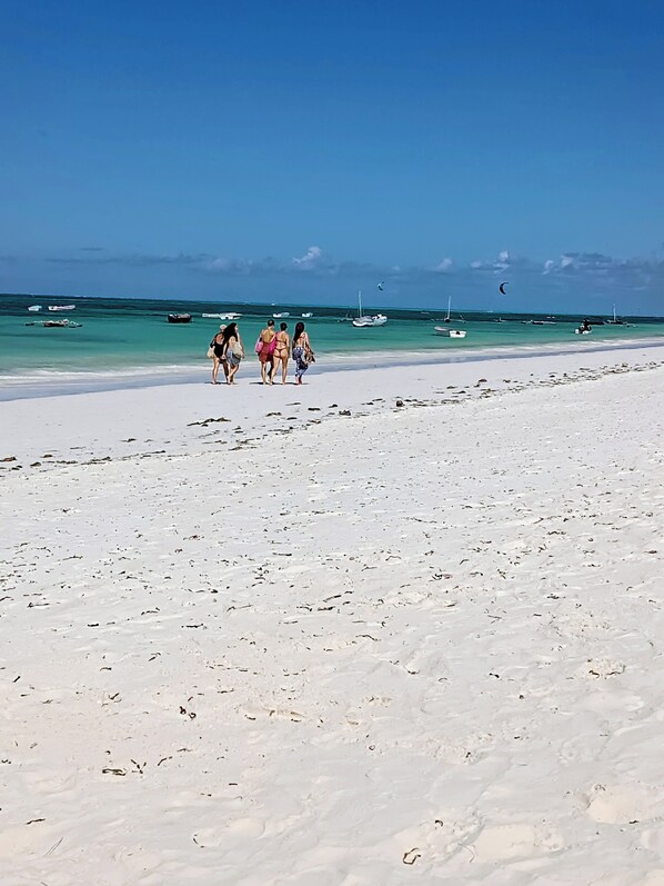 A beach with a clear sky, a few people walking, and boats in the water.