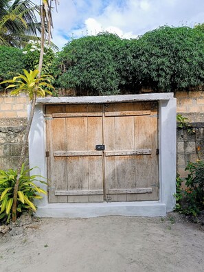 A rustic wooden gate with a metal latch, set in a concrete frame, surrounded by greenery and a brick wall.