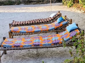 Two wooden lounge chairs with colorful patterned cushions on a sandy surface.