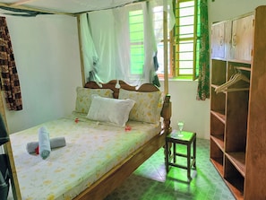 A single bed with a floral bedspread, a bedside table with a glass, and a wooden wardrobe.