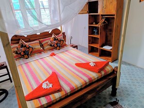 A bed with a striped bedspread, two pillows, a canopy, and a wooden wardrobe with hangers. - Jambiani warm breeze house (Jambiani)