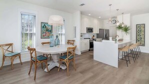 A modern kitchen with white cabinets, a central island with bar stools, and a dining area with a round table and wooden chairs. - 248 Beach Bike Way (Inlet Beach)