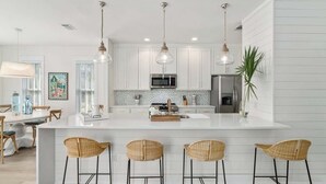 A modern kitchen with white cabinetry, a central island with bar stools, pendant lighting, and a refrigerator. - 248 Beach Bike Way (Inlet Beach)