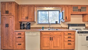 A kitchen with wooden cabinets, a dishwasher, a stove, and a window with a view of trees.
