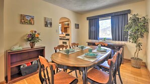 A dining area with a wooden table, chairs, a vase with flowers, and a potted plant.