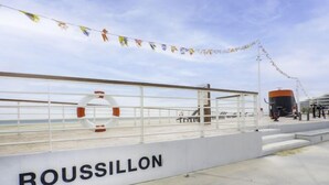 Une plateforme blanche sur laquelle est inscrit le mot « ROUSSILLON » et sur laquelle est posée une bouée de sauvetage.