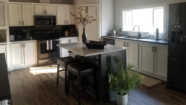 A modern kitchen with white cabinets, a central island, a microwave, a stove, and a refrigerator.