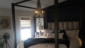A four-poster bed with a dark frame and white bedding, a chandelier, and a bedside table with a lamp.