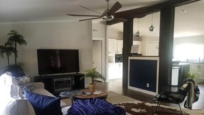 A modern living room with a flat-screen TV, a ceiling fan, a coffee table, and a sofa.