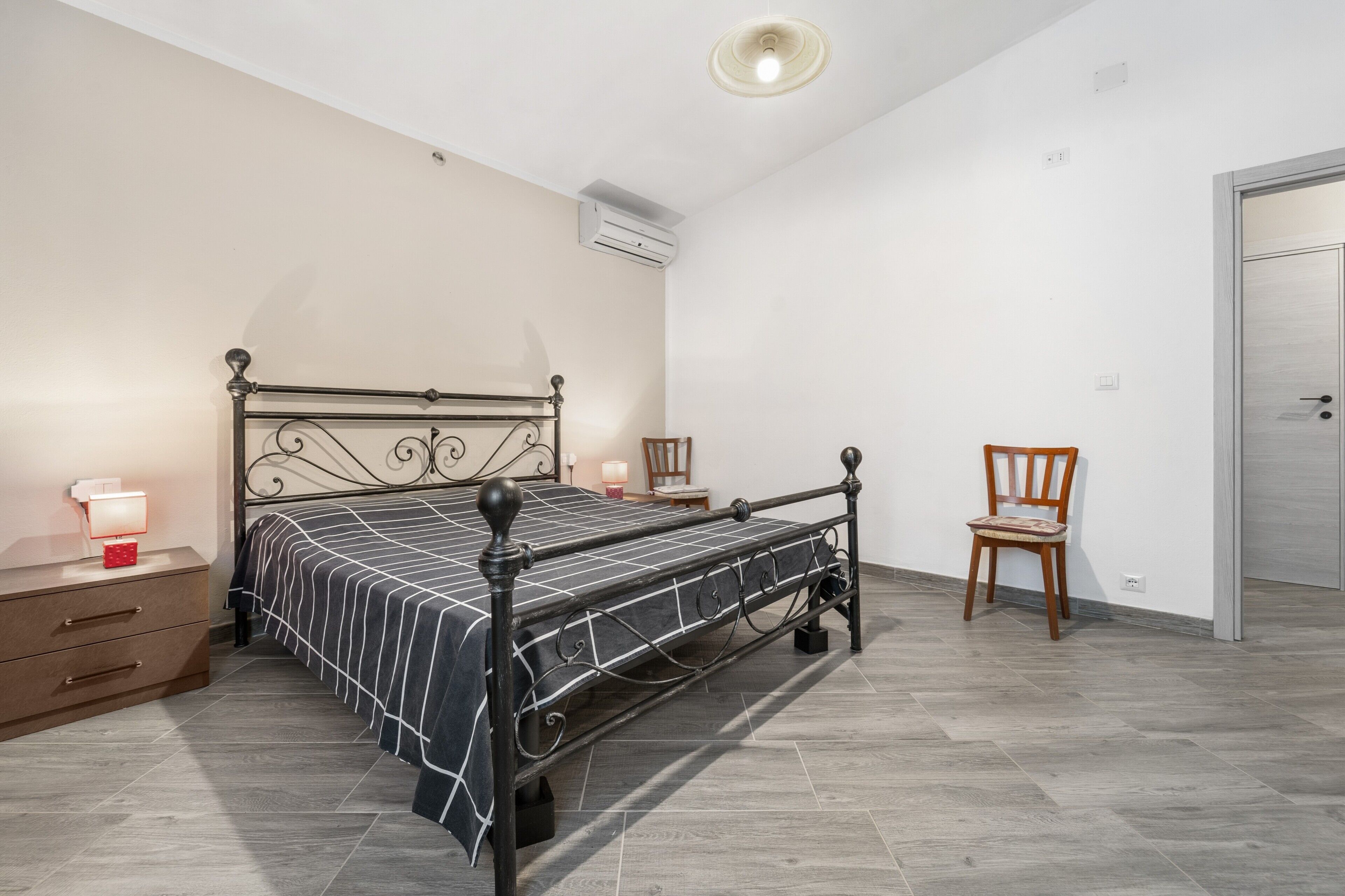 A bedroom with a metal bed frame, a bedside table with a lamp, a chair, and a wardrobe.
