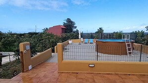 Un área de piscina en la azotea con una escalera, un edificio rojo al fondo y suelo de baldosas.
