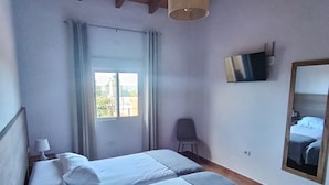 Un dormitorio con dos camas, televisor, espejo y ventana con cortinas.