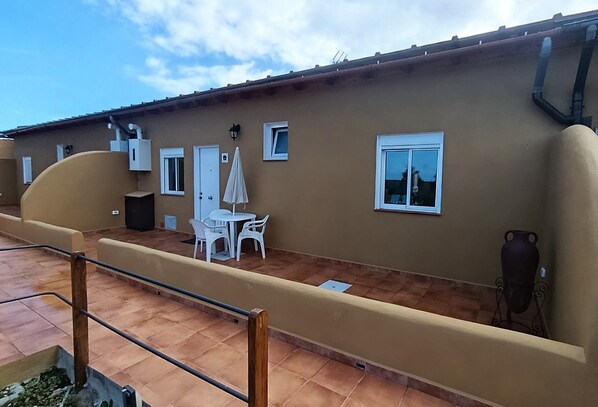 Un edificio con techo plano, una terraza con mesa y sillas, y una puerta blanca.