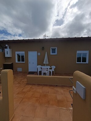 Un patio techado con una mesa, sillas y un pequeño paraguas, además de una puerta.