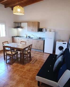 Une cuisine compacte dotée de meubles en bois, d’un four à micro-ondes, d’un lave-linge et d’un coin repas avec une table et des chaises.