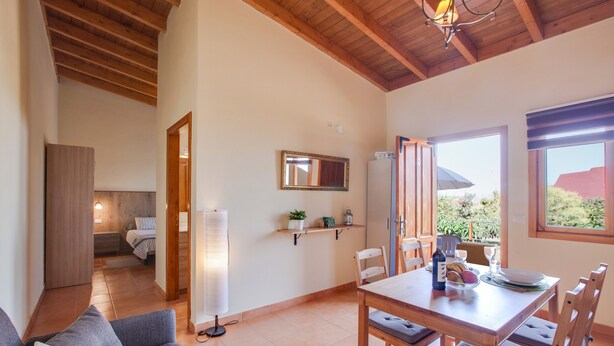 A cozy living area with a sofa, a dining table with chairs, a kitchen area with a refrigerator, and a view through an open door. - Holiday Apartment "Casa Quemahierro 2" with Teide View, Pool and Garden (Icod de los Vinos)