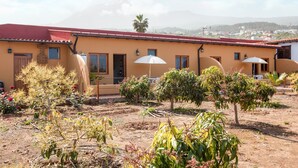 A building with a red roof, multiple windows, and a garden with various plants and trees. - Holiday Apartment "Casa Quemahierro 2" with Teide View, Pool and Garden (Icod de los Vinos)