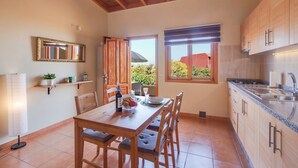 A kitchen with wooden cabinets, a dining table with chairs, a window with a view, and a hanging light fixture. - Holiday Apartment "Casa Quemahierro 2" with Teide View, Pool and Garden (Icod de los Vinos)