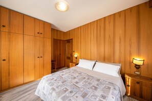 A bedroom with wooden panel walls, a bed with a patterned bedspread, two bedside lamps, and a nightstand. - Appartamento Primavera 1 with Mountain View, Wi-Fi, Balcony & Garden (Moena)