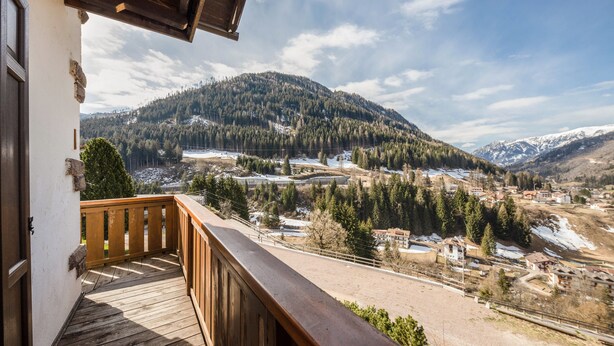 A wooden balcony with a view of a mountainous landscape, including snow-covered peaks and a valley with buildings. - Appartamento Primavera 1 with Mountain View, Wi-Fi, Balcony & Garden (Moena)