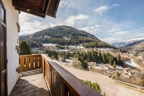 A wooden balcony with a view of a mountainous landscape, including snow-covered peaks and a valley with buildings. - Appartamento Primavera 1 with Mountain View, Wi-Fi, Balcony & Garden (Moena)