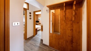 A hallway with wooden doors, a light switch, and a view into a bedroom with a bed and a desk. - Appartamento Primavera 1 with Mountain View, Wi-Fi, Balcony & Garden (Moena)