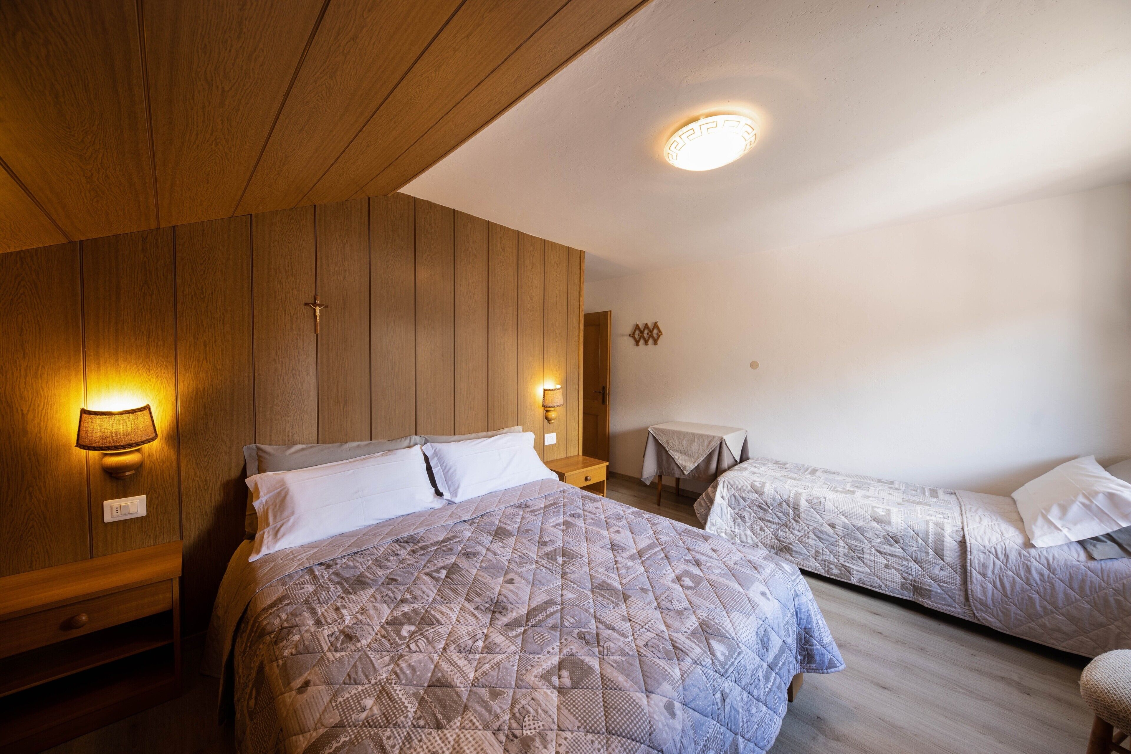 Une chambre d’hôtel avec un grand lit, deux tables de chevet, une lampe fixée au mur et un luminaire au plafond.