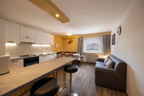 A modern kitchen with a bar area, a dining table, and a sofa in a living area.