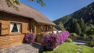 Uma cabana de tronco com alicerce de pedra, fachada de madeira e varanda com caixas de flores.