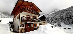 Un chalet en bois doté d’un balcon, entouré d’arbres et de montagnes couverts de neige.