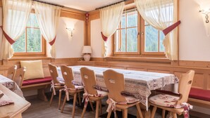 A cozy room with wooden walls, a dining table with chairs, and large windows with curtains. - Vacation Chalet Crepes De Sela with Mountain View, Wi-Fi, Balcony & Garden (Canazei)