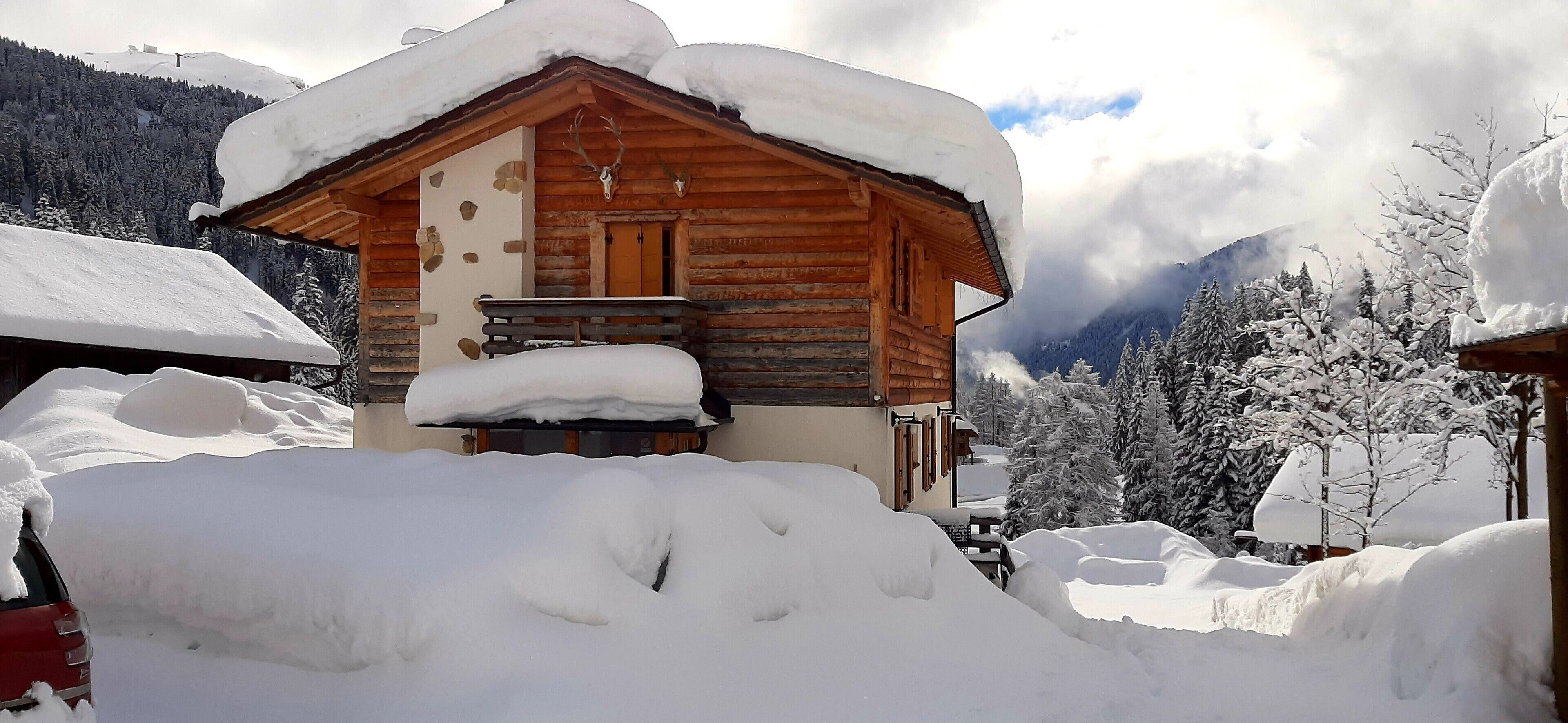 Une cabane en bois avec un toit enneigé, un mur en pierre et une porte en bois.