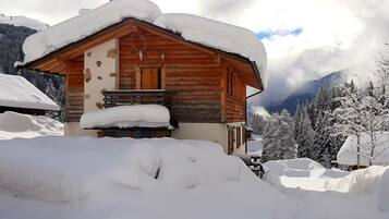 Une cabane en bois avec un toit enneigé, un mur en pierre et une porte en bois.