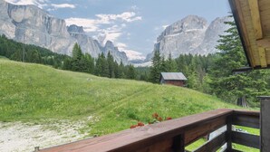 A wooden deck with a view of a mountain landscape, a small cabin, and a forested area. - Vacation Chalet Crepes De Sela with Mountain View, Wi-Fi, Balcony & Garden (Canazei)