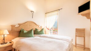 A double bed with a wooden headboard, a bedside table with a lamp, and a window with curtains. - Vacation Chalet Crepes De Sela with Mountain View, Wi-Fi, Balcony & Garden (Canazei)