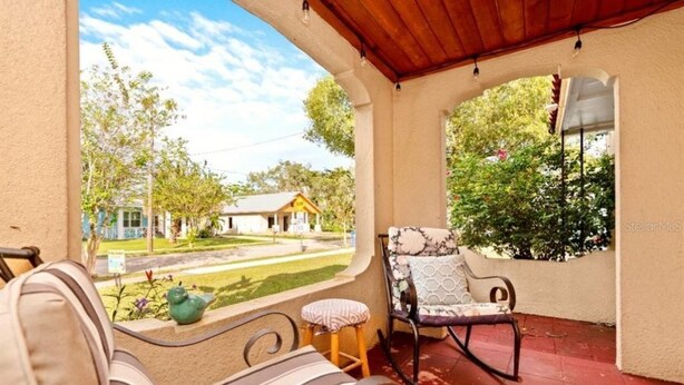 A covered patio with a view of a residential area, featuring a striped sofa, a rocking chair, and a small stool. - Close to Downtown, LECOM Field, AMI Beaches and more (Bradenton)