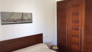 A bedroom with a wooden bed, a nightstand, a wardrobe, and a framed picture on the wall. - Holiday Apartment Apartamento Llenaire with Pool, Wi-Fi, A/C, Garden, Terrace & Balcony; Parking Available (Pollensa)