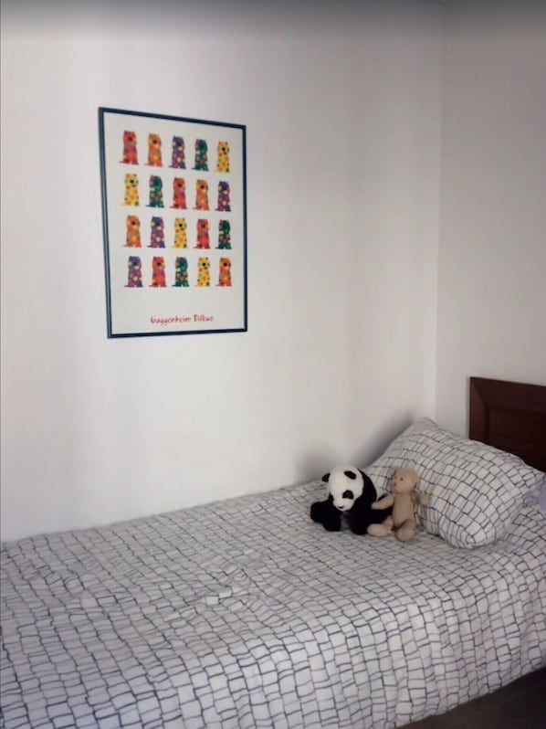 A bed with a patterned bedspread, a framed picture of colorful teddy bears on the wall, and a panda and teddy bear on the bed.