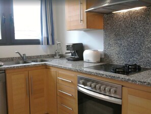 A kitchen with granite countertops, stainless steel appliances, wooden cabinets, and a window with curtains.