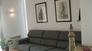 A living room with a grey sofa, a small table with a plant, a remote control, and a lighthouse model. - Holiday Apartment Apartamento Llenaire with Pool, Wi-Fi, A/C, Garden, Terrace & Balcony; Parking Available (Pollensa)