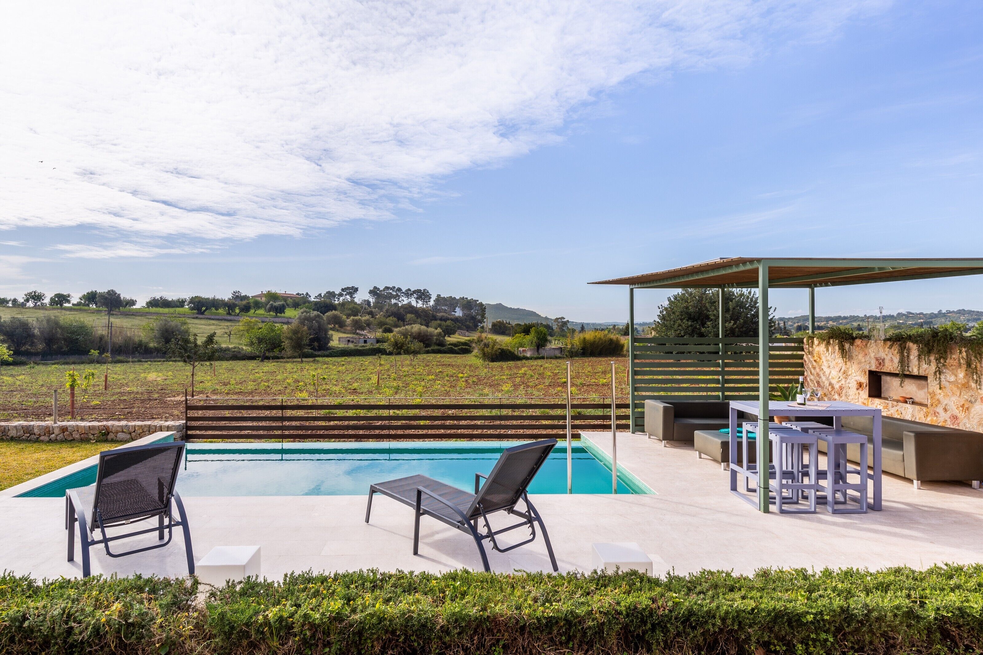 A poolside area with two lounge chairs, a table, and a covered seating area.