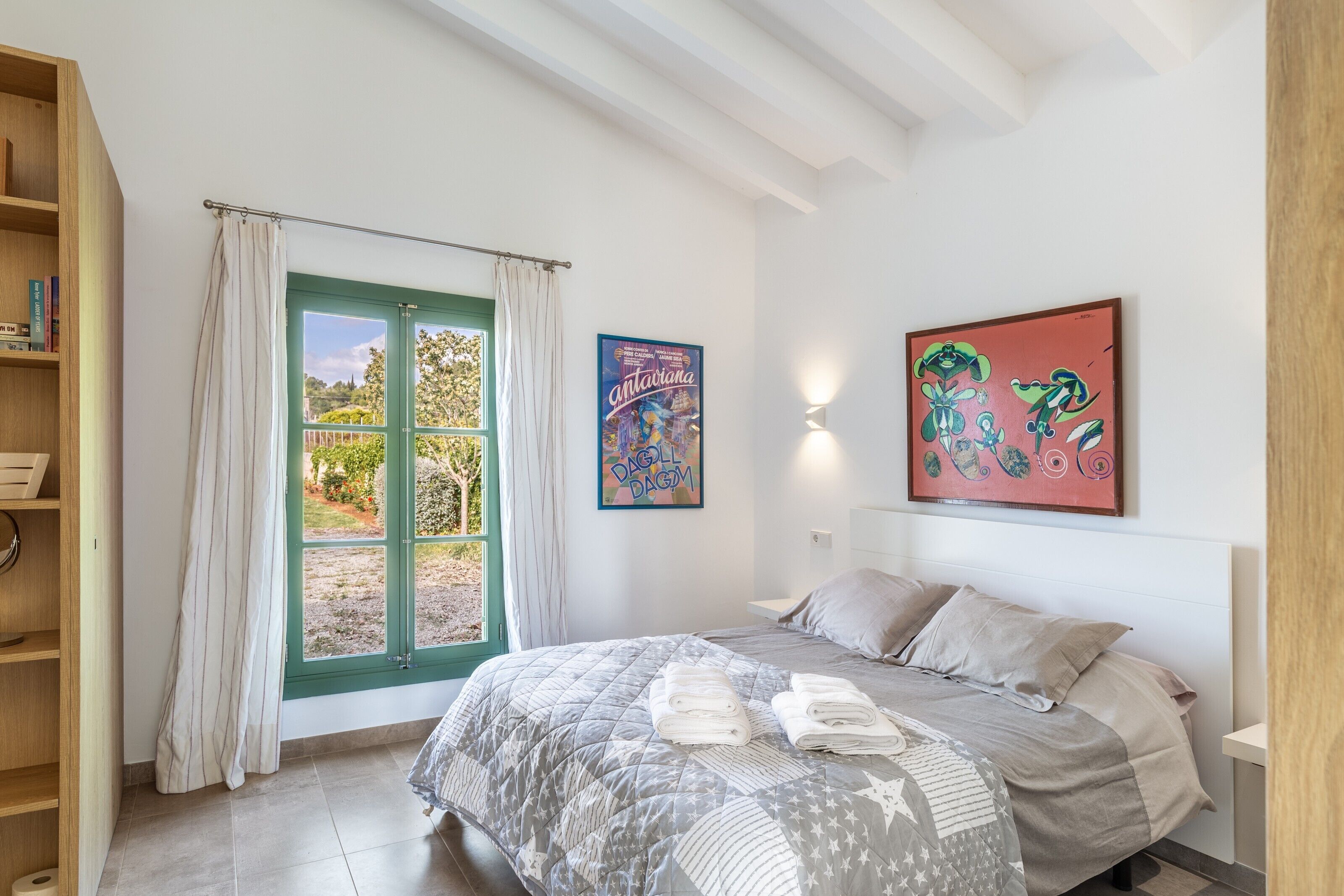 A bedroom with a bed, a window with curtains, a wall with a poster, and a bookshelf.