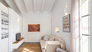Una sala de estar moderna con un sofá, una televisión, una obra de arte en la pared y una ventana con cortinas.