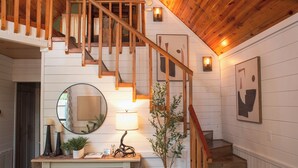 Una escalera con barandillas de madera y una pared blanca con un espejo y una lámpara.