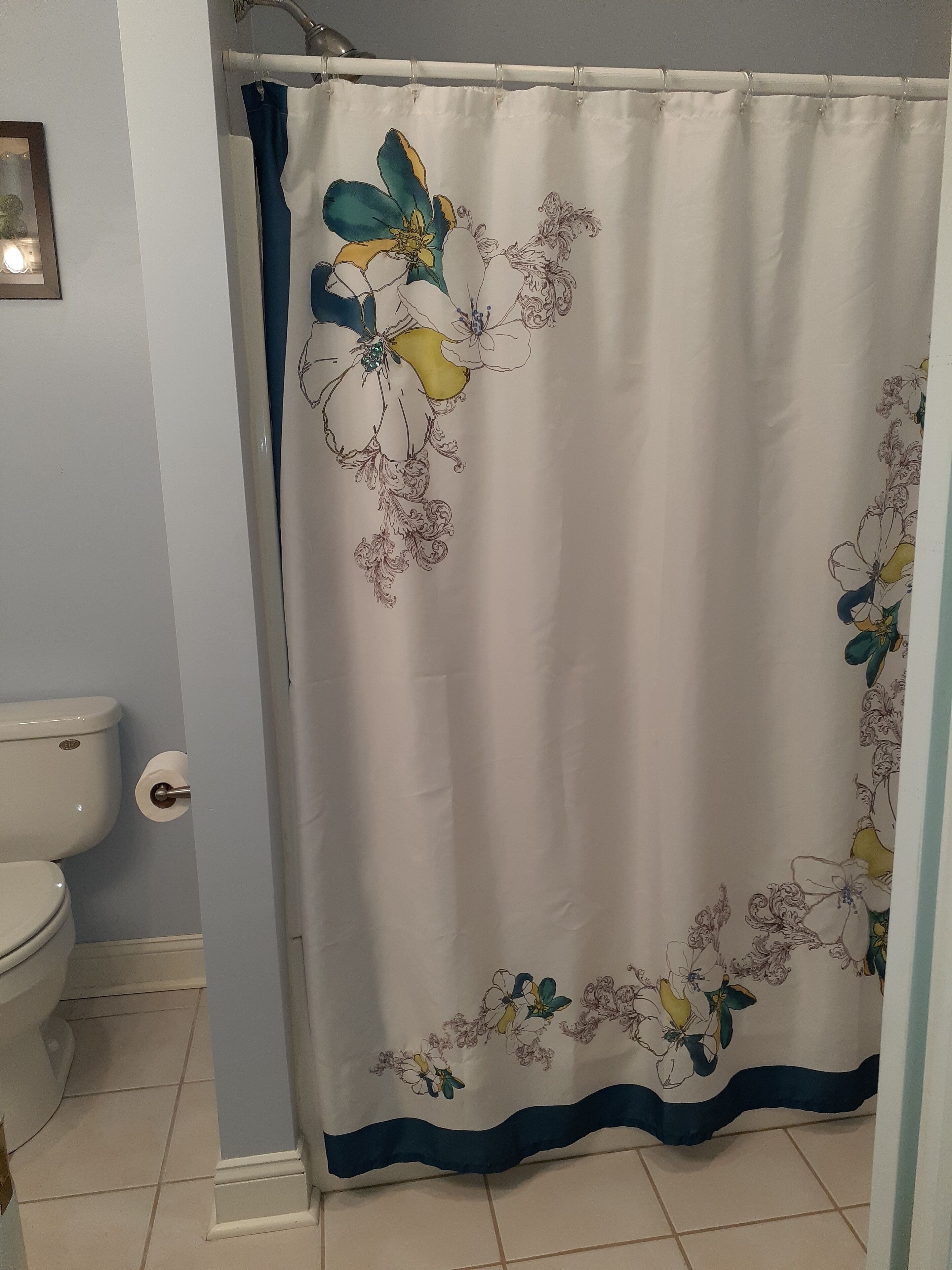 Un baño con inodoro blanco, cortina de ducha con motivos florales y pared azul claro.