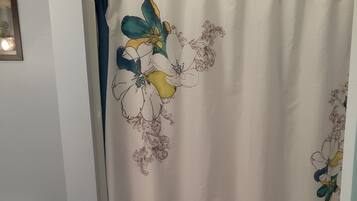 Un baño con inodoro blanco, cortina de ducha con motivos florales y pared azul claro.