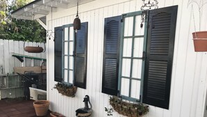 A white building with two windows, each with black shutters, and a hanging light fixture. There are potted plants on the windowsill and a barrel on the ground. - ENJOY THE HISTORY, NOSTALGIA AND CULTURE OF OLD TOWN MERIDIAN (Meridian)