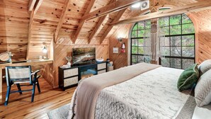 Dormitorio de cabaña de madera con cama, escritorio, silla y ventanas amplias.