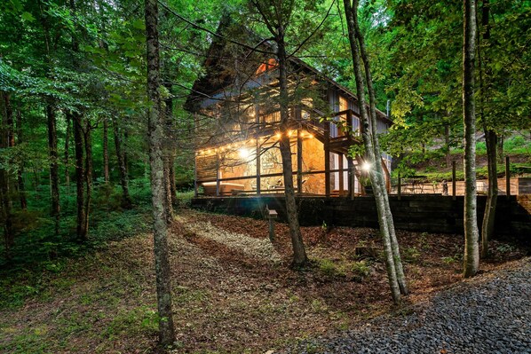 A cabin surrounded by trees with a wooden deck and a stone wall.