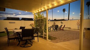 Una terrazza esterna con tavolo e sedie, luci a catena e vista sul cielo.